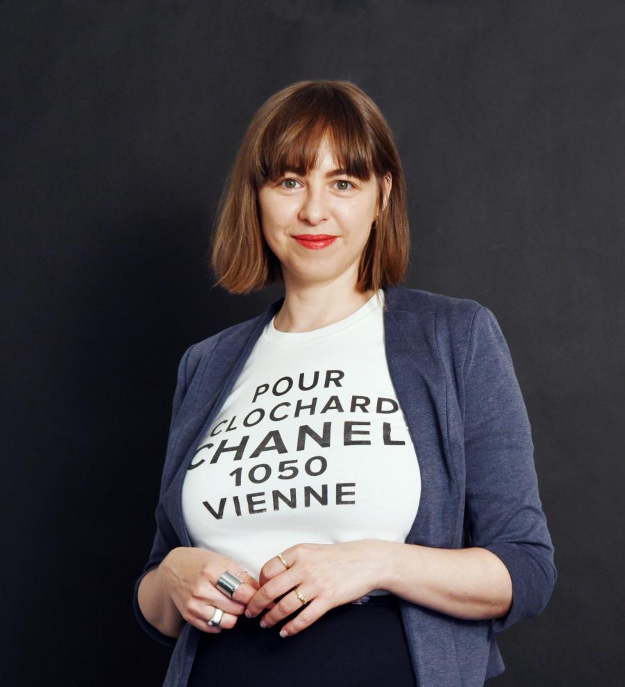 Photo of Johanna Mayr-Keber in front of a dark background. She wears a tshirt with the words "pour chlochard chanel 1050 vienne", which is by the artist Martin Grandits.